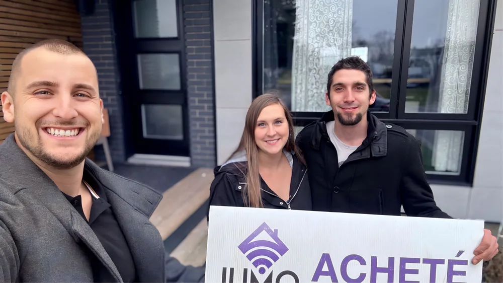 Couple client de Jumo Immobilier avec la pancarte « Acheté » devant leur nouvelle maison